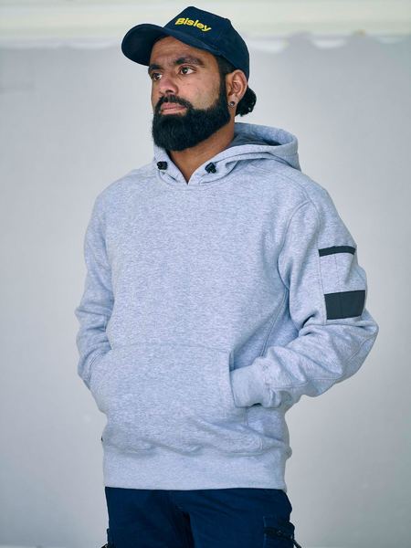 Man wearing a light gray Bisley hoodie with black arm patches and a navy cap against a plain background